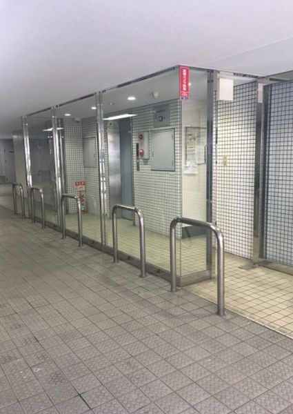 MIWAファーストビルのエントランスホール。ガラスの自動ドアにタイル張りの外壁、ステンレスの駐輪ラックが並ぶビル1階の入口。