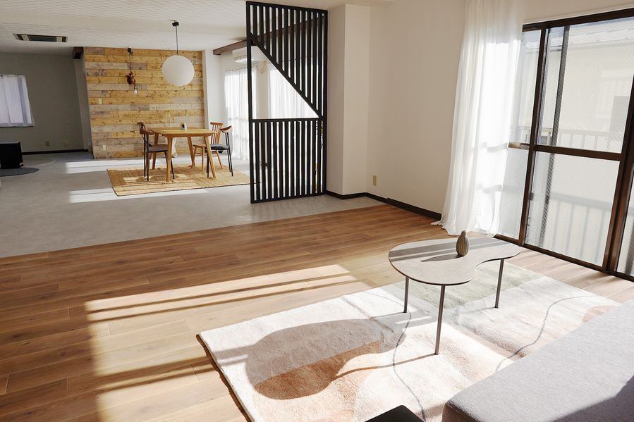 フローリングのリビングゾーンから、黒い縦格子パーティション越しにコンクリート床のダイニングゾーンを見渡す。奥の壁にはパイン材の古材が横張りされ、白い和紙ペンダントライトが空間のアクセントになっている。