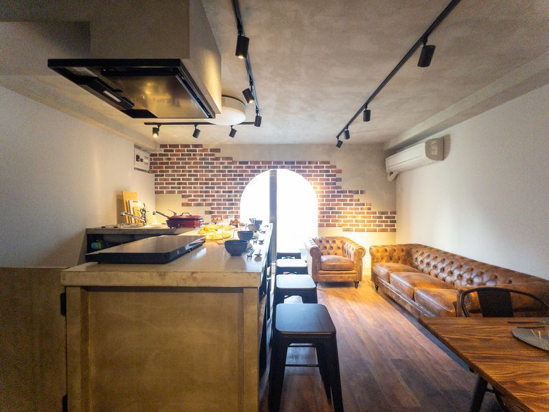 カウンターキッチンでの調理風景。IHコンロの上に鍋やフライパンが並び、奥にはBRUNOホットプレートと料理が見える。アーチ窓からの逆光がカウンター全体を柔らかく照らしている。