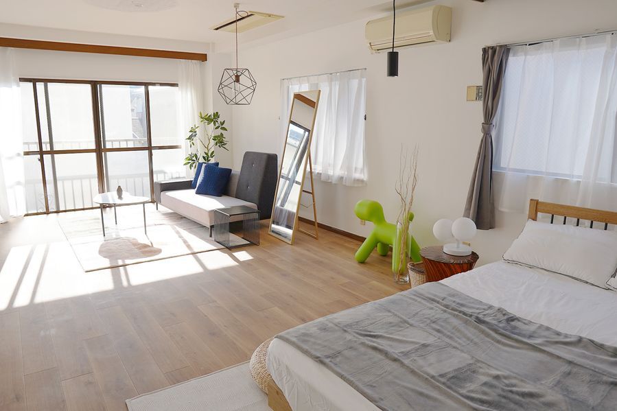 木製フレームのセミダブルベッドに白いリネンとグレーのブランケット。窓辺にはライムグリーンのマジス・パピーチェア、ラタンのバスケット、丸い畳クッション。小窓から柔らかい光が入り、ナチュラルで温かみのあるベッドルームシーンが完成している。