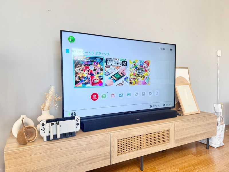 ラタン編みのテレビボードの上に50インチ大型テレビ。画面にはNintendo Switchのマリオカート8デラックスのホーム画面が映し出されている。テレビの下にはサウンドバー、脇にSwitch本体とドック。