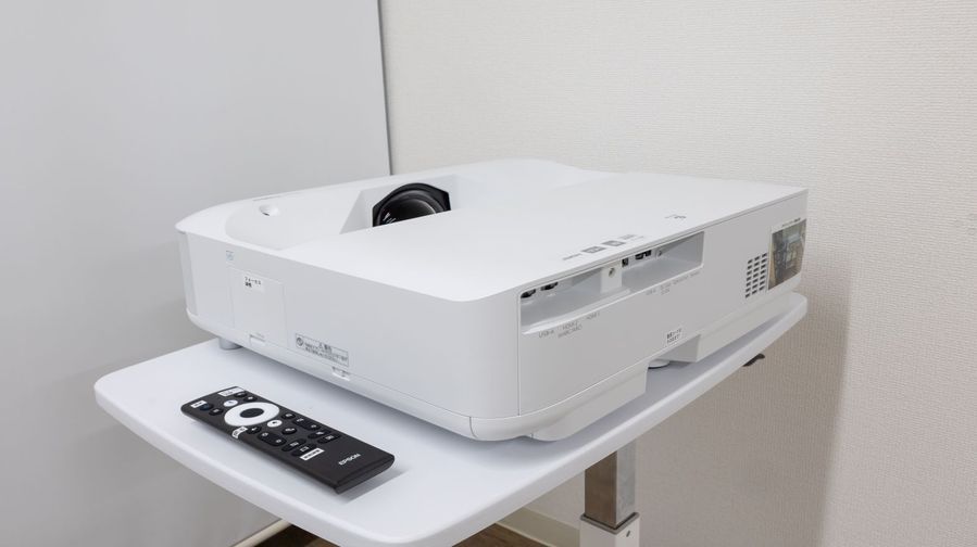 EPSON EH-LS650W 4Kプロジェクターのクローズアップ。白いスタンドの上に本体と専用リモコンが置かれている。3,600ルーメンの高輝度レーザーモデル。